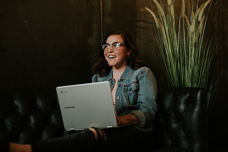 donna sorridente seduta sul divano con in mano un computer portatile