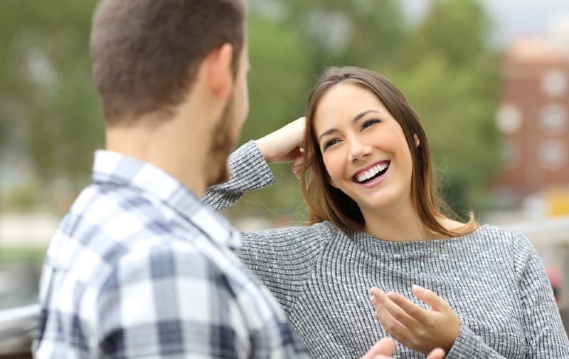Giovane donna sorridente che parla con un uomo seduto accanto a lui all'aperto