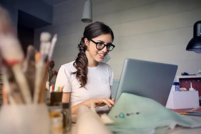 smiling woman using her laptop wearing eyeglasses and white shirt
