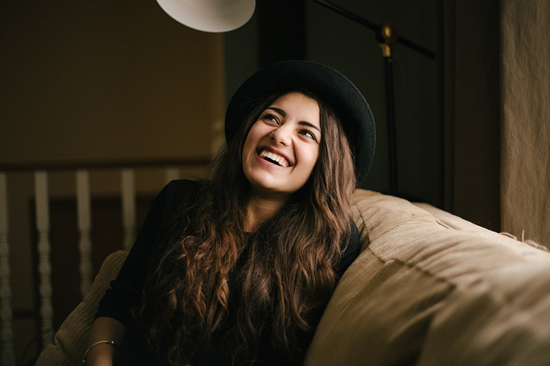 donna sorridente con cappello nero seduta sul divano