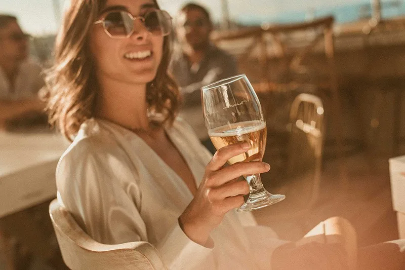 smiling woman wearing sunglasses while holding glass of wine