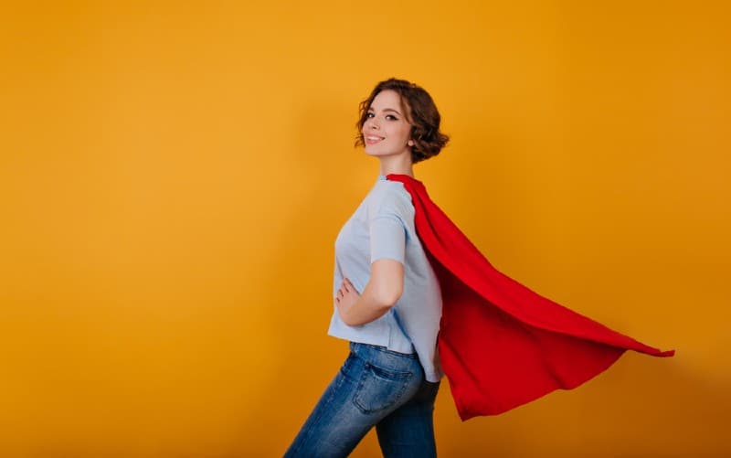 Joven mujer sonriente con vaqueros azules y capa de superhéroe