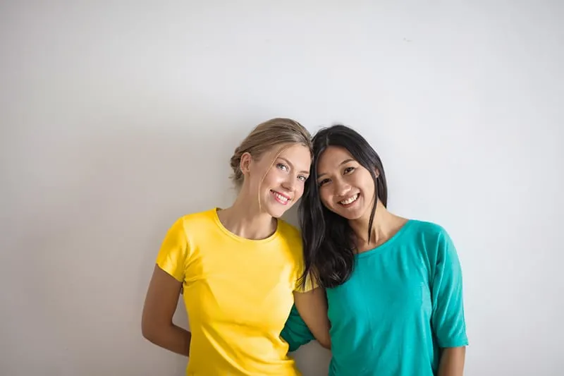 smiling women in yellow and blue t-shirts leaning on each other