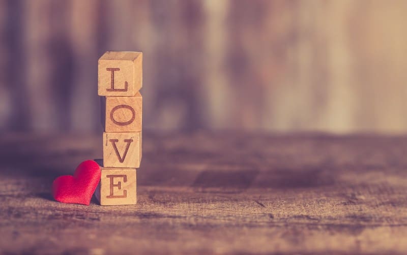 Stack of love wooden blocks near a small red heart