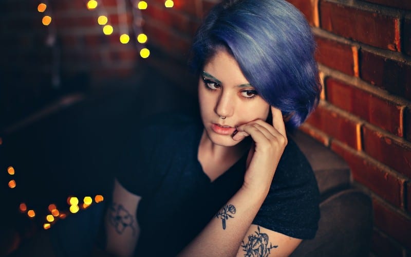 thinking tattooed woman with blue hair wearing black t-shirt