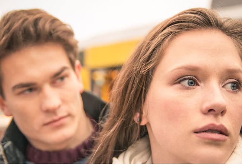 teary eyed woman in focus and a man behind her