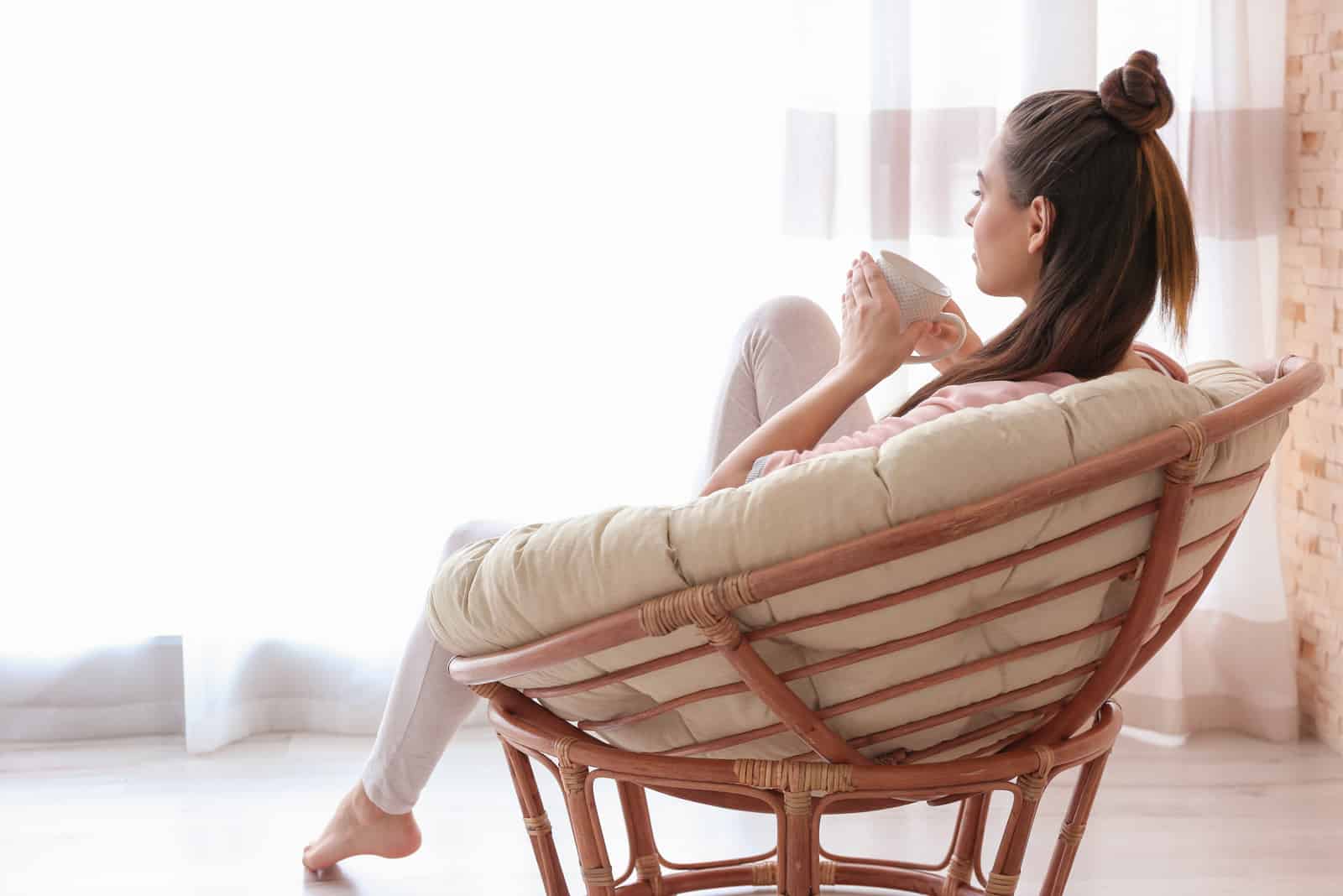 la mujer está sentada en una silla bebiendo café y mirando al frente