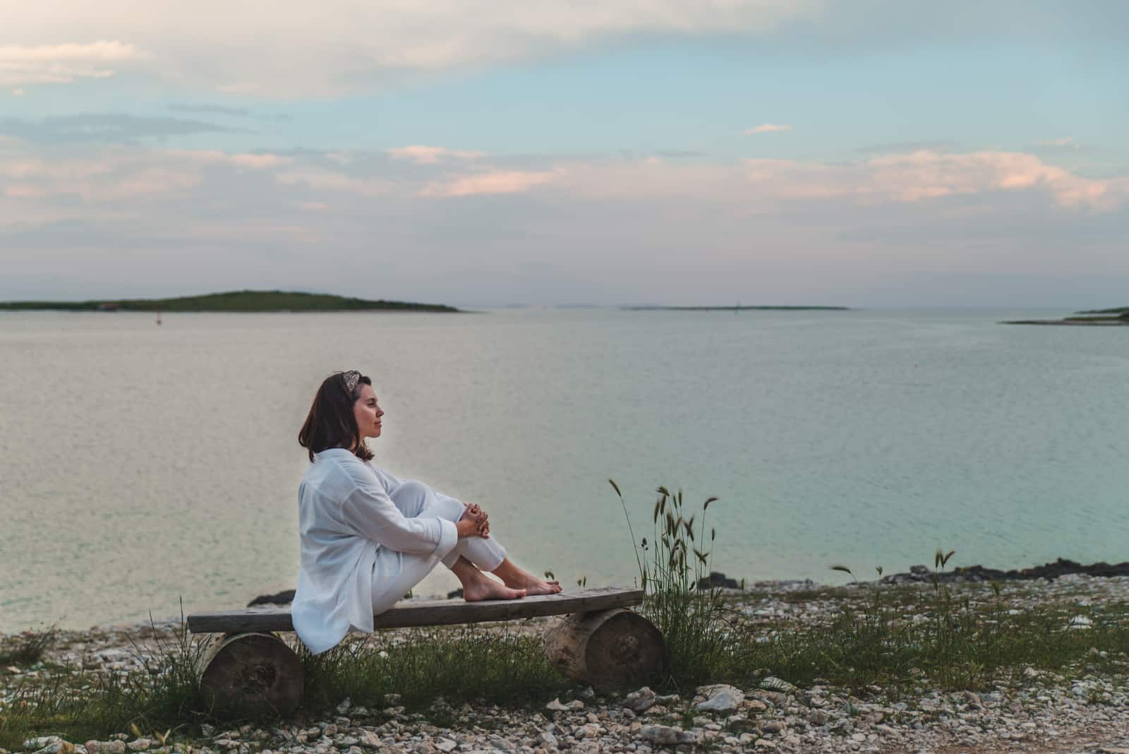 la donna siede in riva al mare su una panchina e guarda di fronte a sé
