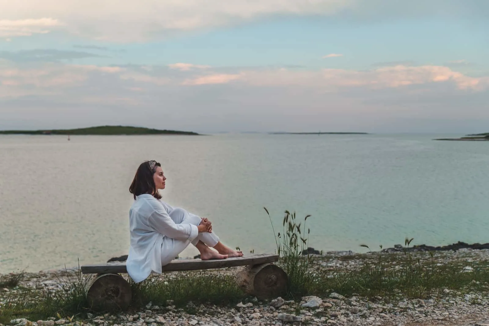 the woman sits by the sea on a bench and looks in front of her