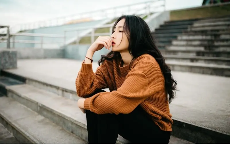 Thinking asian woman sitting on stairs outdoors during daytime