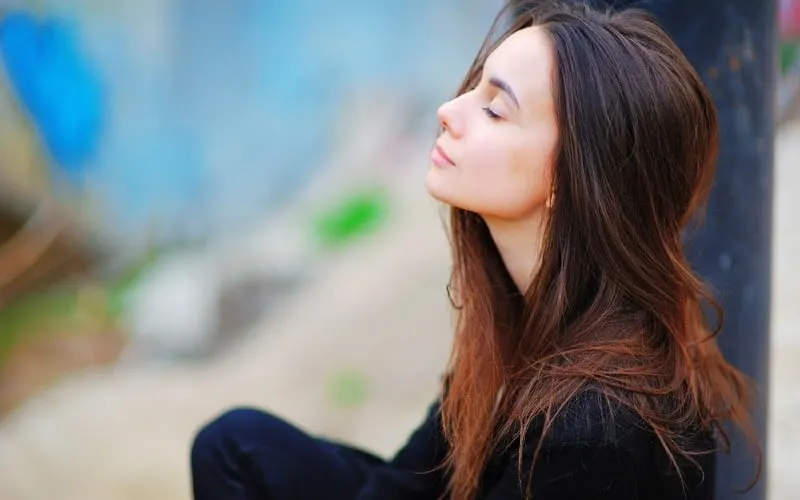 Thinking young woman with her eyes closed sitting outdoors