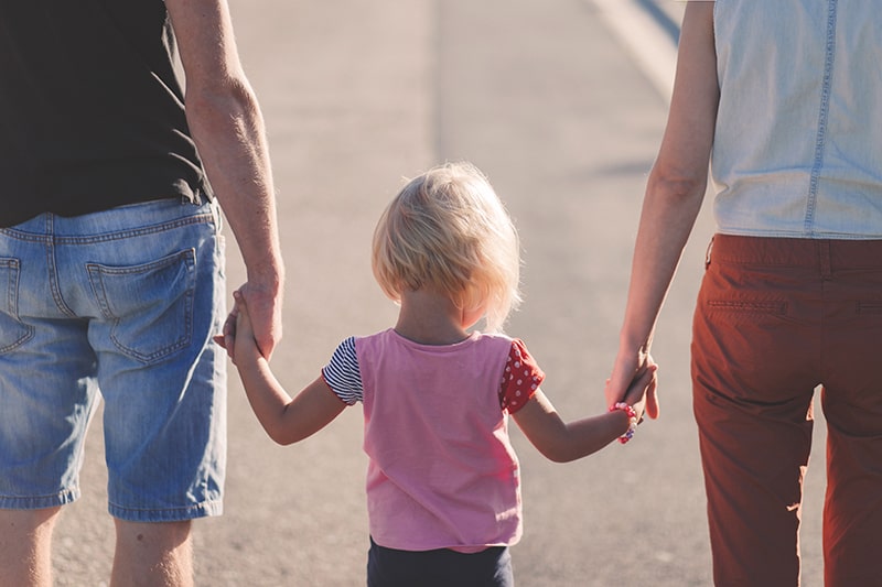 bambino con camicia rosa che tiene per mano i genitori