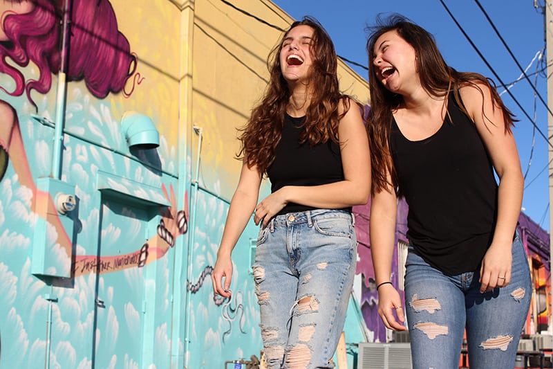 two laughing women walking past grafitti wall