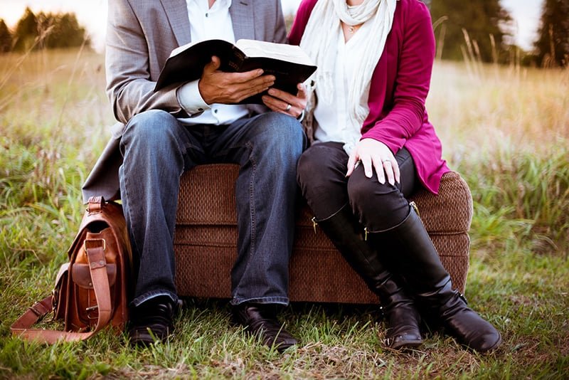two people sitting beside each other while reading a book