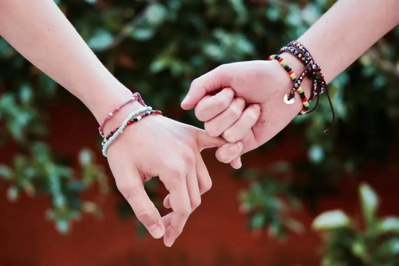 two person with bracelets holding pinky fingers