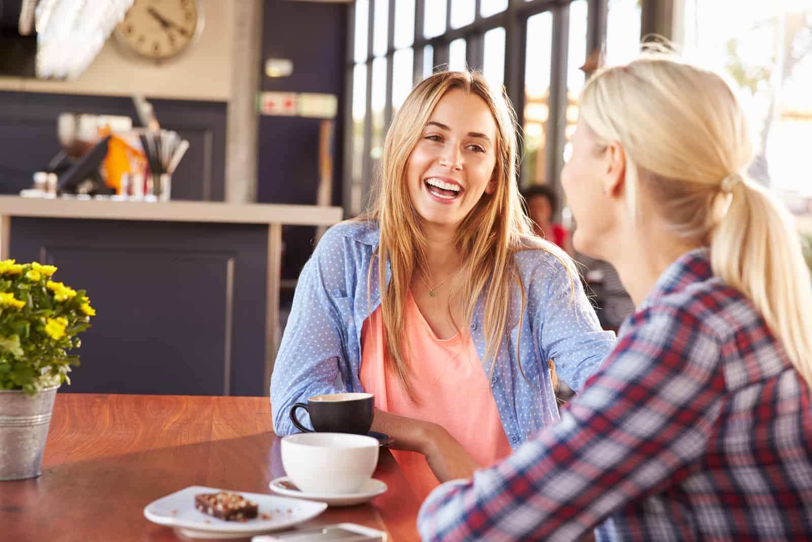 two smiling friends sit and talk over coffee