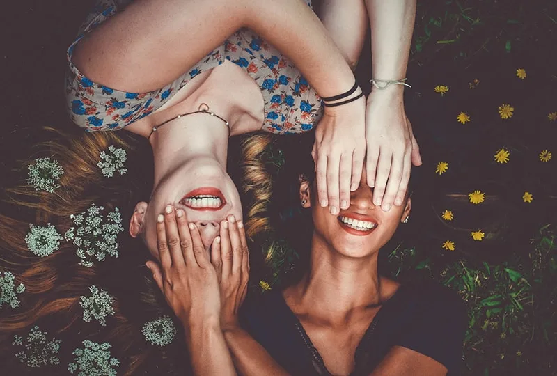two women hiding face with palm while lying on lawn field