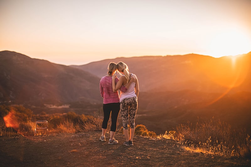 two women hugging on the mountain during the sunset