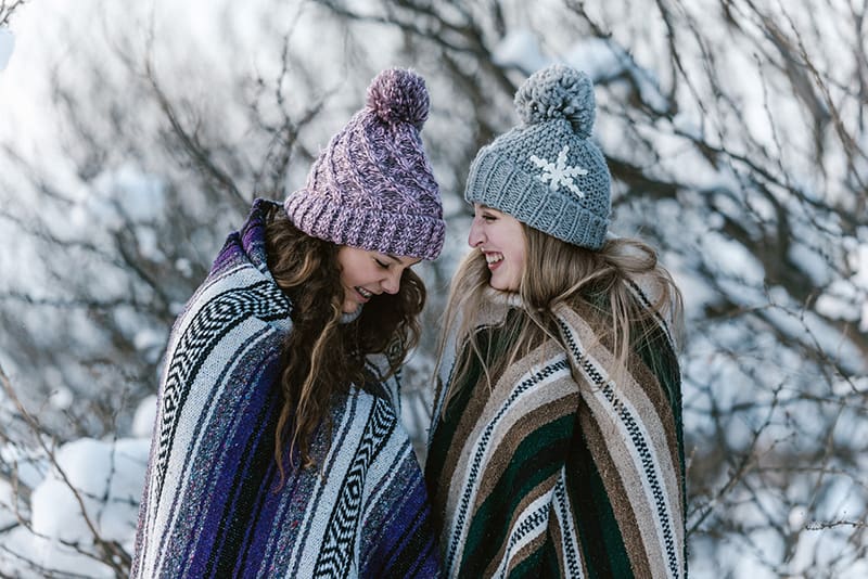 duas mulheres com um cobertor às riscas multicoloridas perto de uma árvore