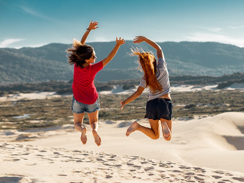 two women jumping high on sand