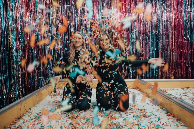 two women kneeling while throwning confetti over them