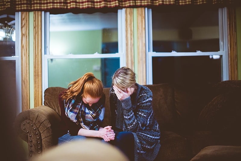 two women sitting on sofa in a room while crying