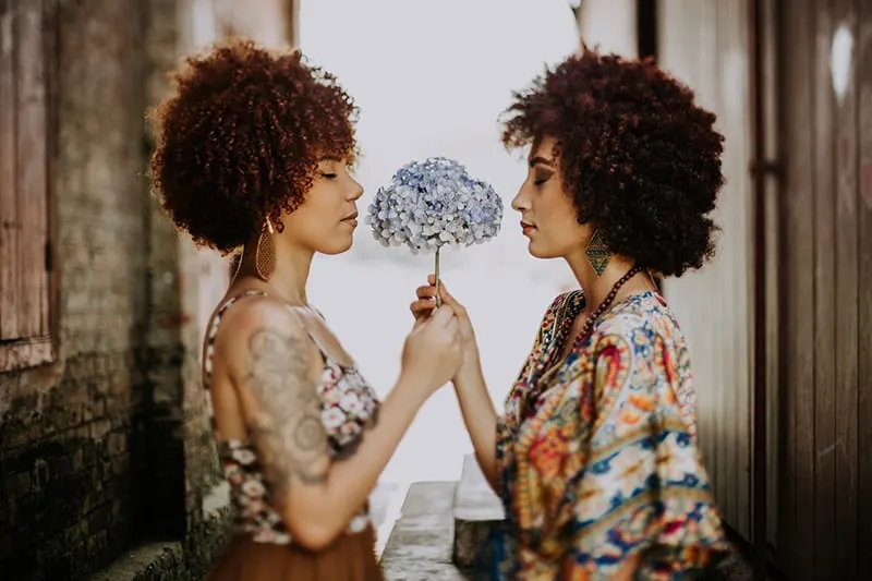 two women with afro hair holding flower together