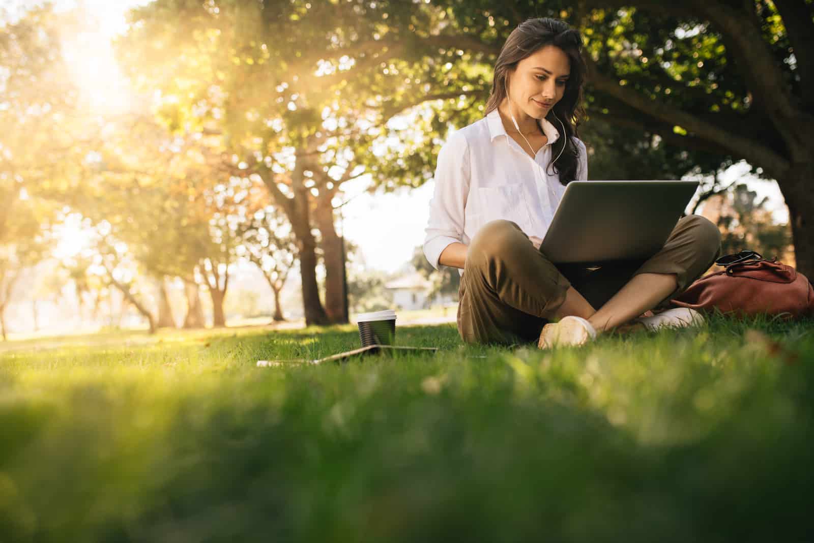 une belle jeune femme assise sur l'herbe et en tapant sur un ordinateur portable
