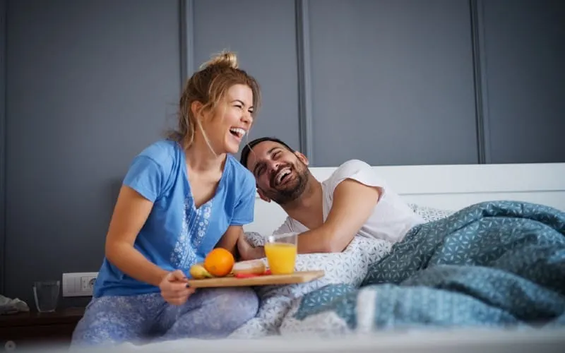 Laughung wife bringing breakfast to her husband lying in bed