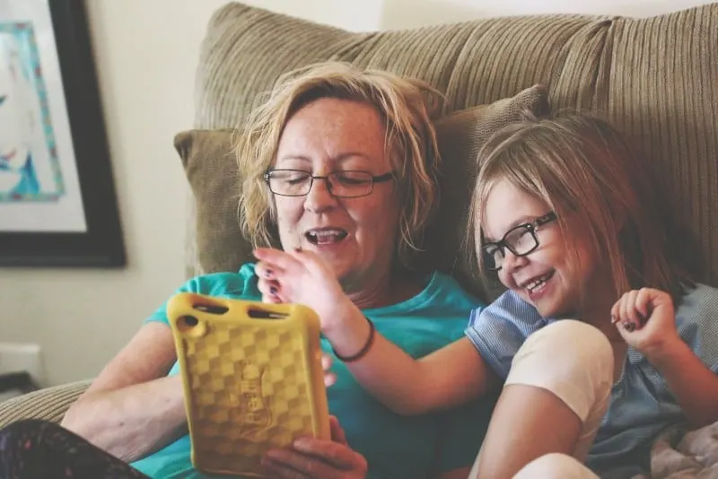 woman and girl sitting on sofa and using tablet