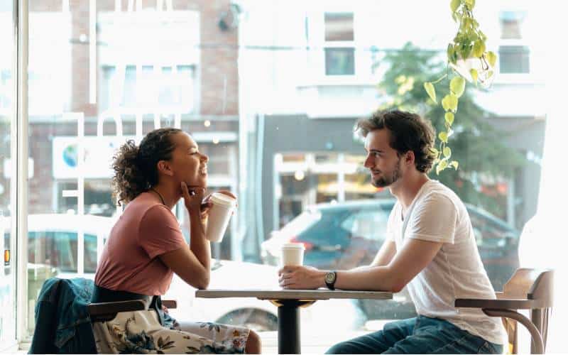 Mulher e homem a beber café e a conversar numa mesa junto a uma janela durante o dia