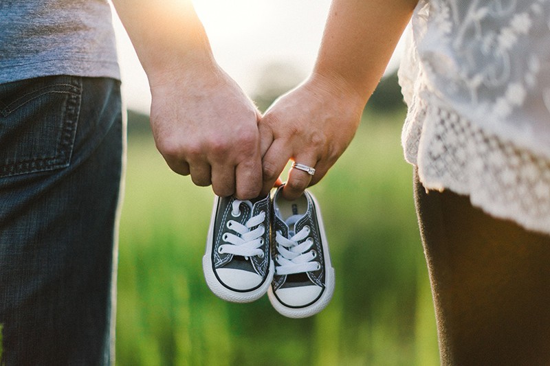 woman and man holding black crib shoes standing near green grass