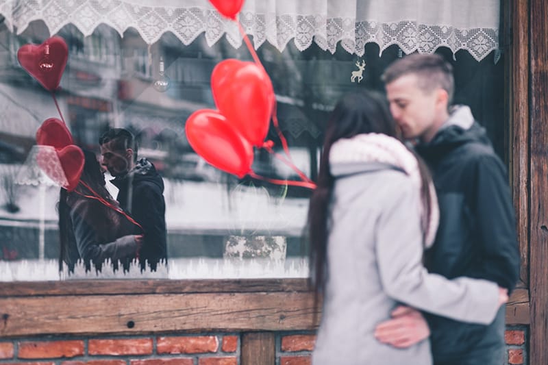 mujer y hombre besandose delante de la tienda y sosteniendo globos rojos