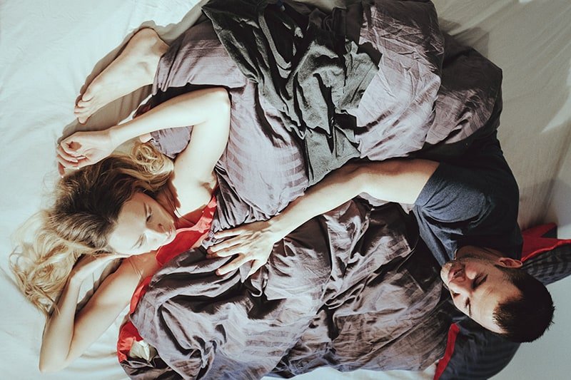 woman and man lying on bed covered with gray sheets