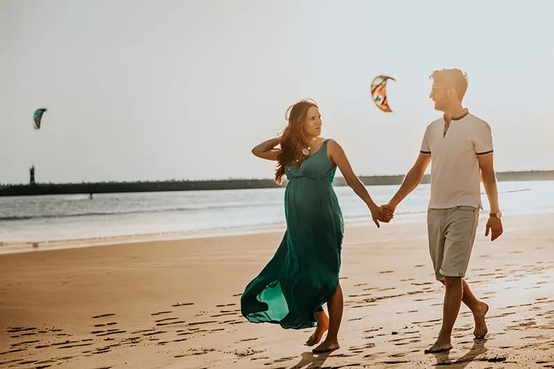 woman and man walking on beach while holding hands
