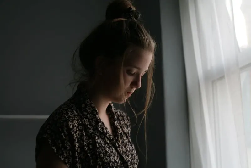 sad woman standing beside window curtain