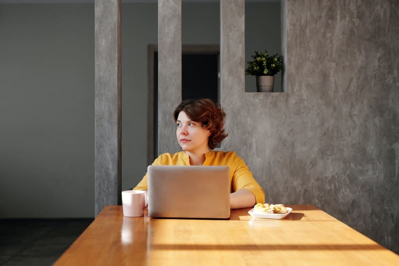 donna al laptop che guarda lontano con i pensieri vaganti