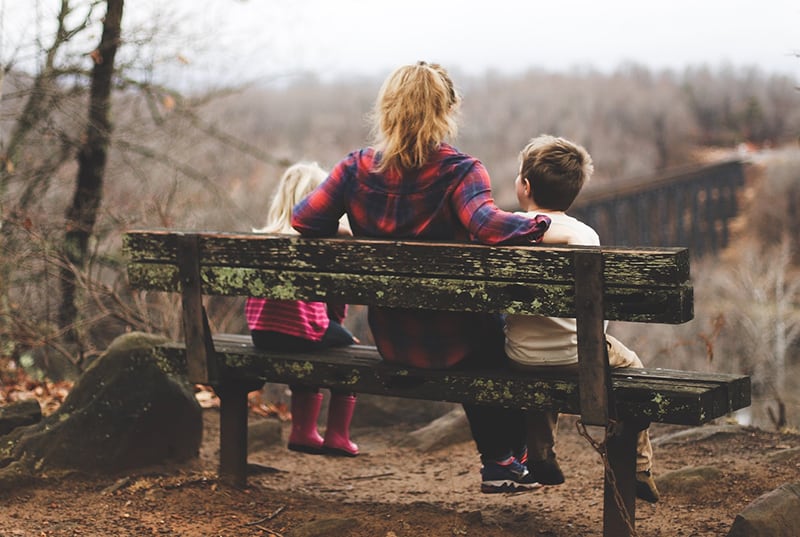 donna tra due bambini seduti su una panchina di legno marrone