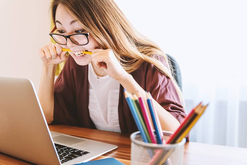 Woman biting pencil while staring at laptop