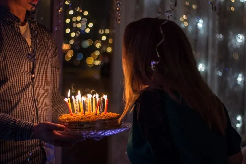 woman blowing out candles while man holding birthday cake