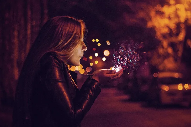 woman blowing sprinkle in her hand while standing in the night