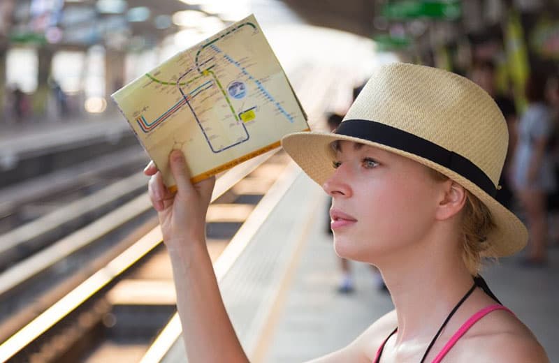 donna che porta una mappa e indossa un cappello in piedi vicino a una ferrovia