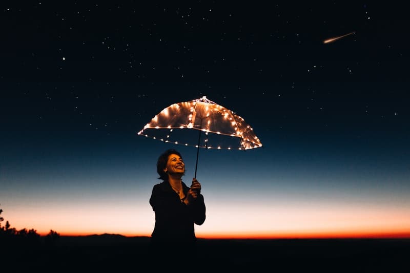 mulher carregando um guarda-chuva com luzes numa noite estrelada 