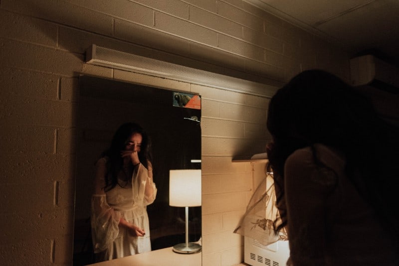 donna in abito bianco che piange davanti allo specchio