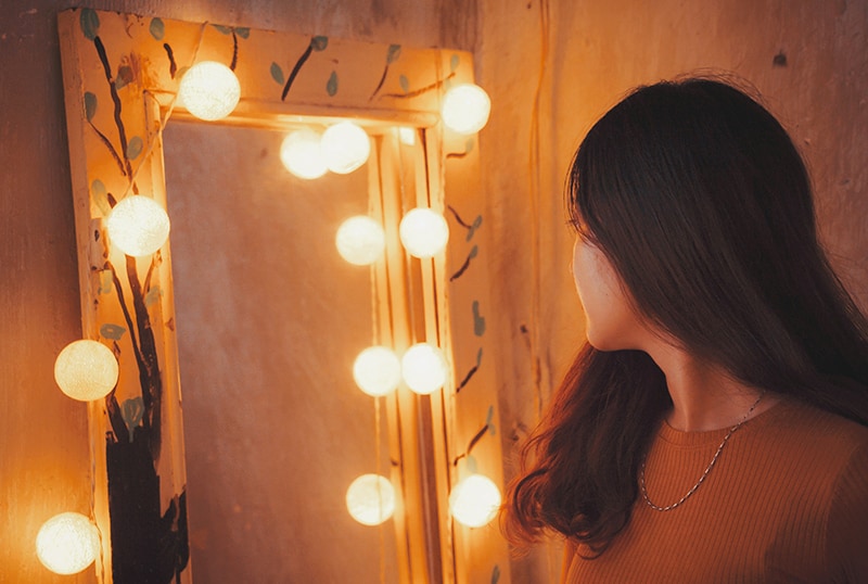 woman facing mirror surrounded with lights