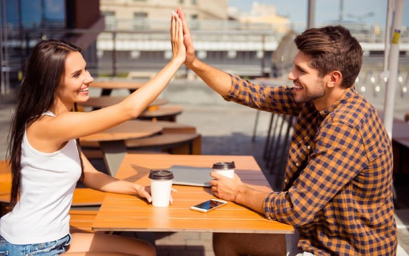 Mujer feliz chocando los cinco con un hombre sentado en una mesa al aire libre durante el día.