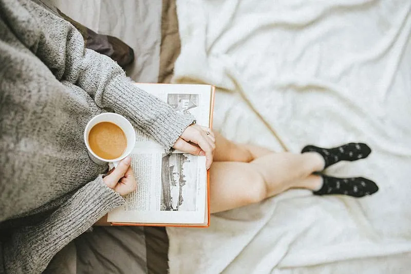 Woman in grey sweater holding coffee cup and reading a book