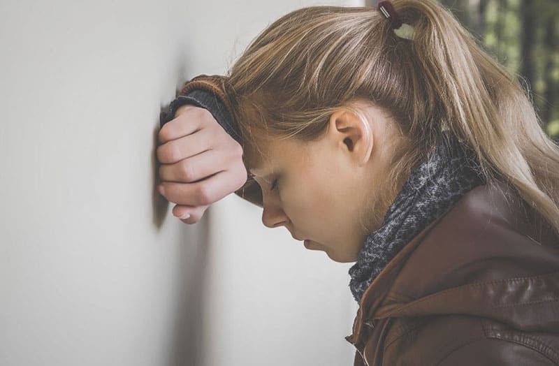 mujer cabeza sobre brazos apoyada en pared blanca