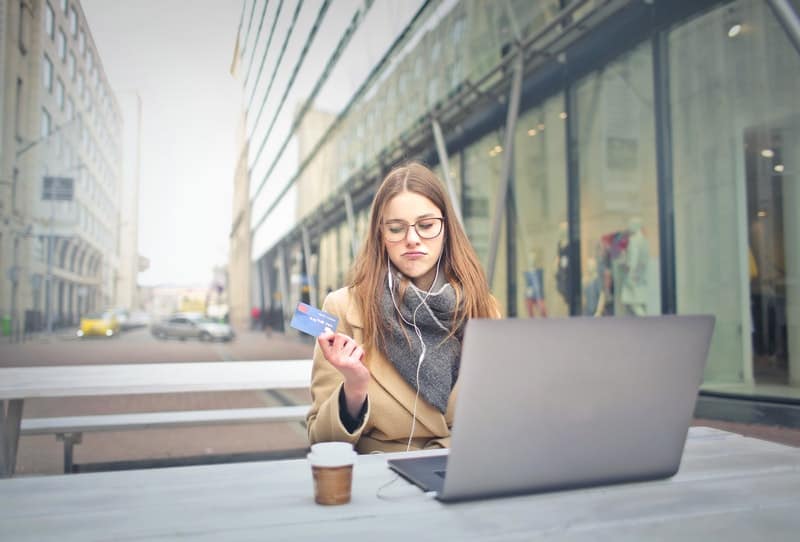 woman holding a bank card wearing brown coat having coffee