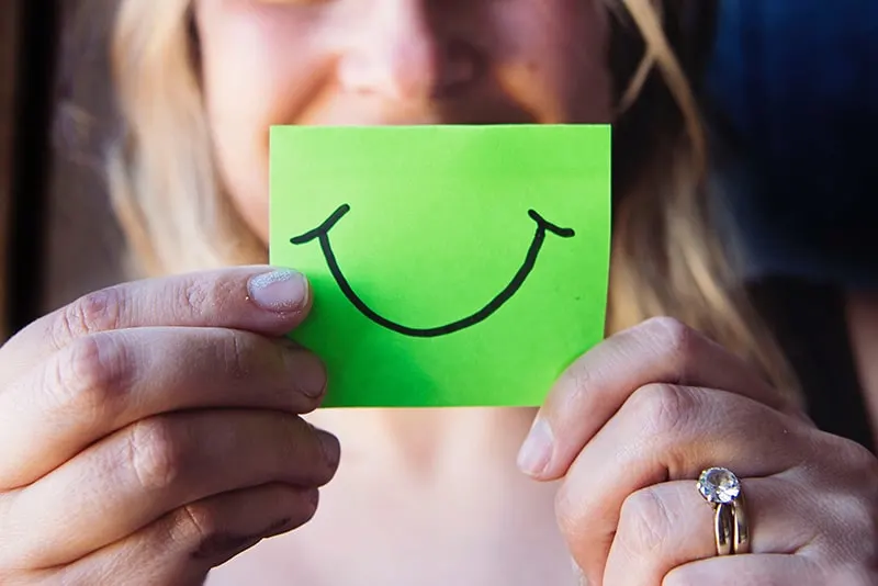 woman holding a green paper with smile drawn on it 